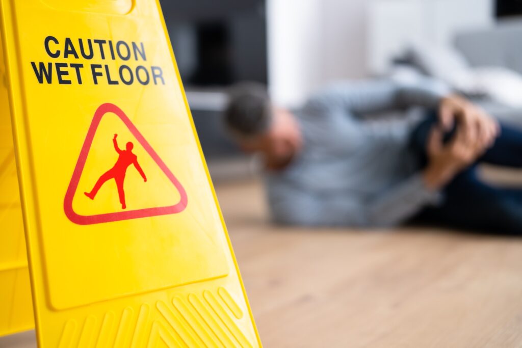 Wet Floor Caution Sign and a Person on the Background Holding Their Knee